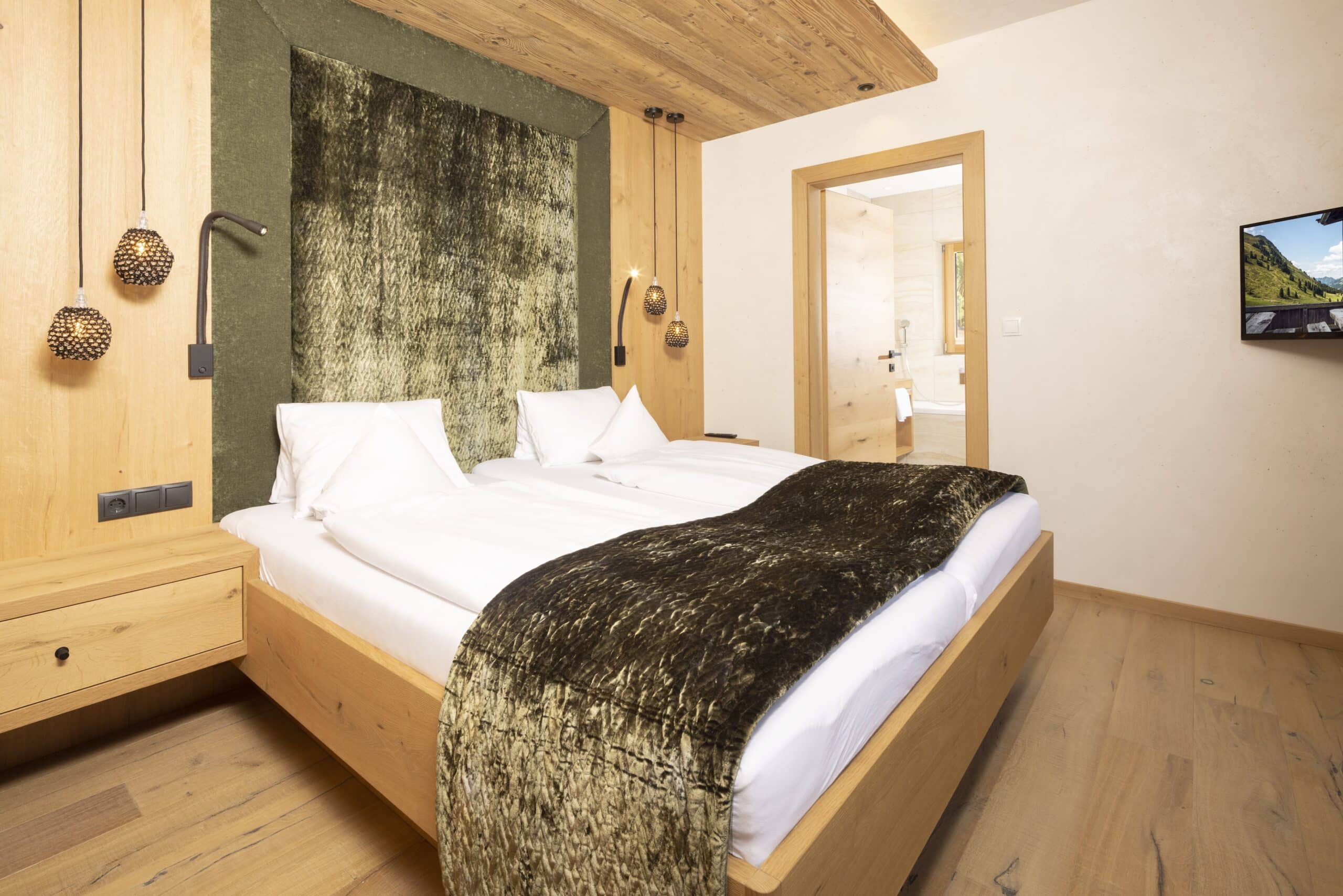 Ein gemütlich eingerichtetes Schlafzimmer mit einem großen Doppelbett, weißer Bettwäsche und hölzernen Möbeln. An der Wand hängen dekorative Lampen.