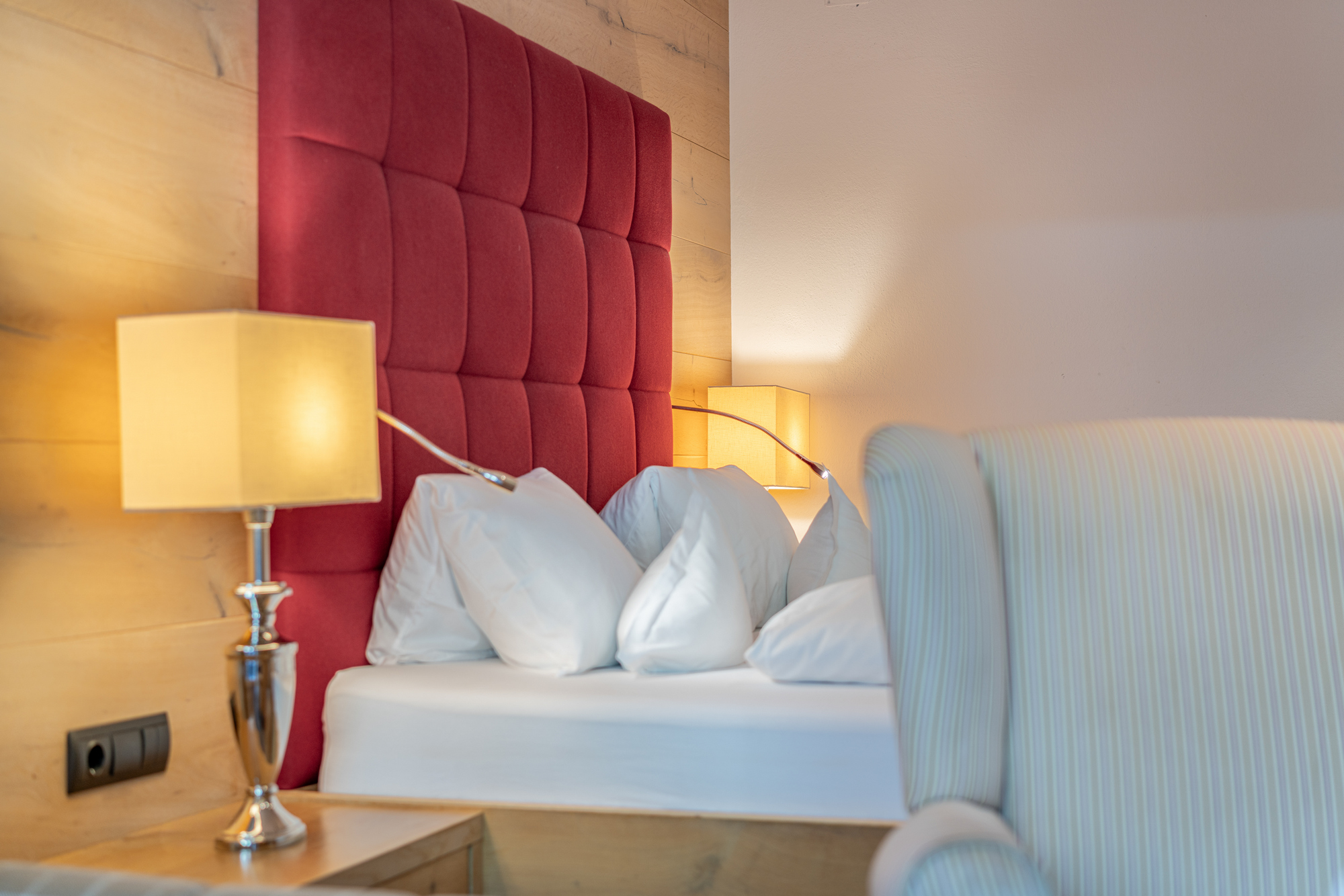 Bett mit weißen Polstern und roter Rückwand auf Holz, zwei Stehlampen