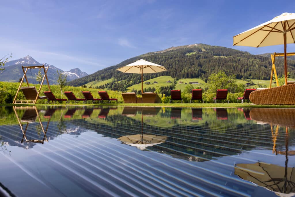 Sommertag_adults Only Pool-rote Liegen und helle Sonnenschirme mit Blick auf die grünen Berge