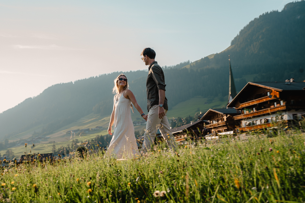 Pärchen spaziert hand in hand durch wiese, Hintergrund Häuser und Kirchturm
