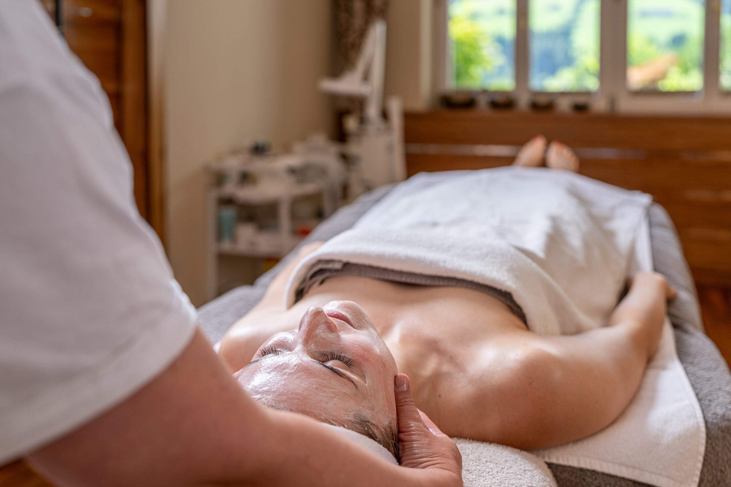 Frau auf dem Rücken liegend auf Massageliege im weißen Handtuch_Therapeutin