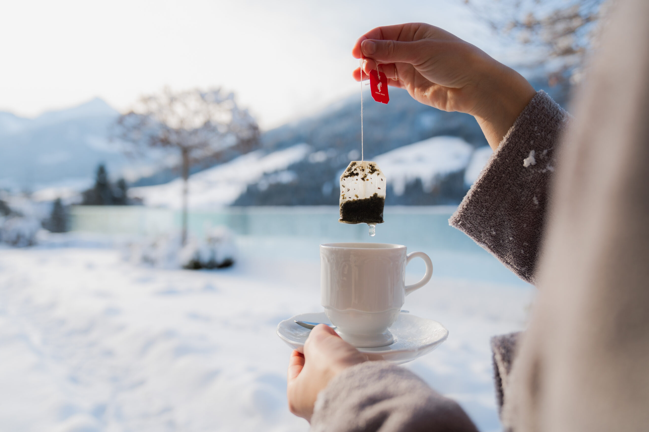 Frau mit Tee am Outdoorpool vor Bergpanorama