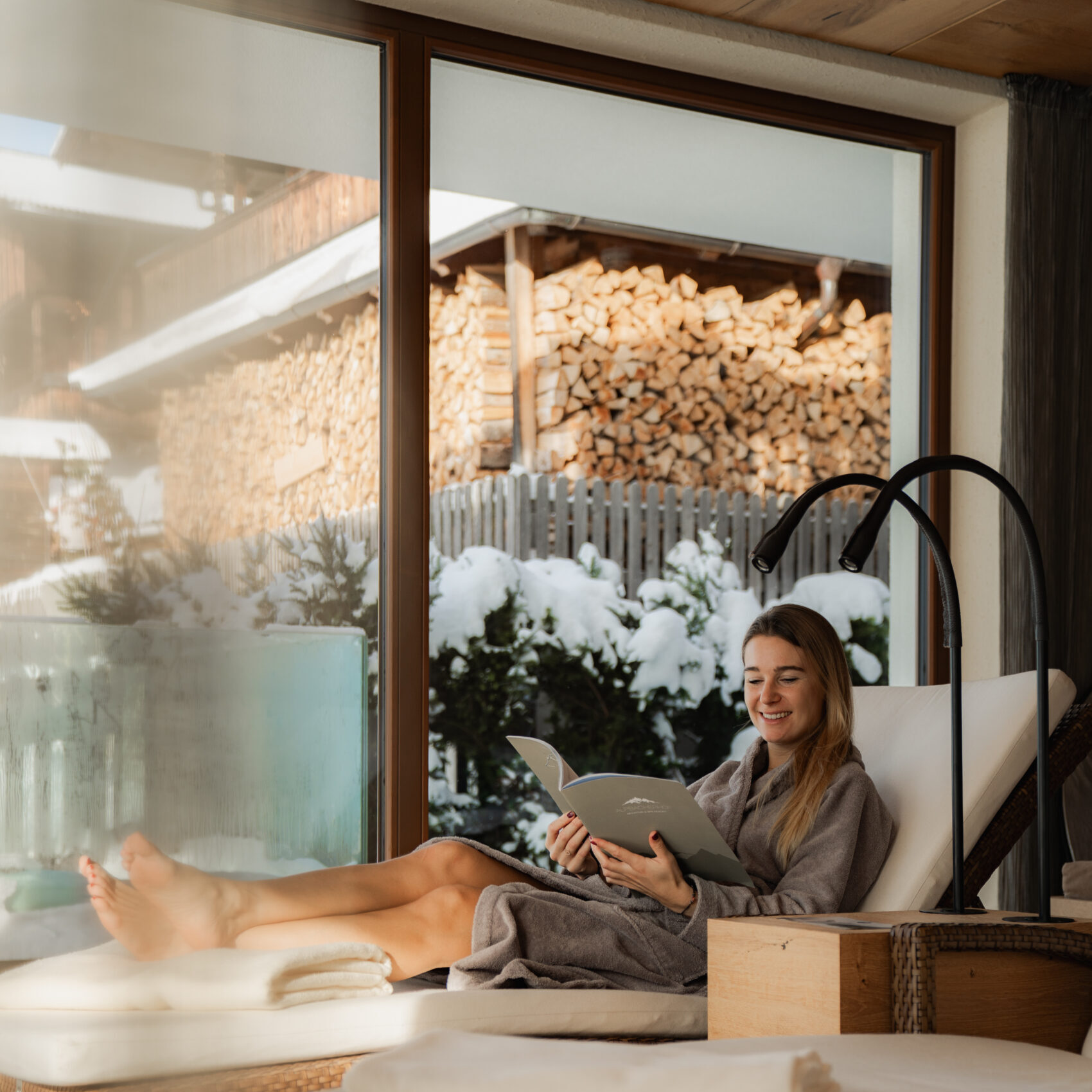 Frau liest Broschüre im Relax Room des Wellnesshotels Alpbacherhof, im Hintergrund tief verschneiter Garten