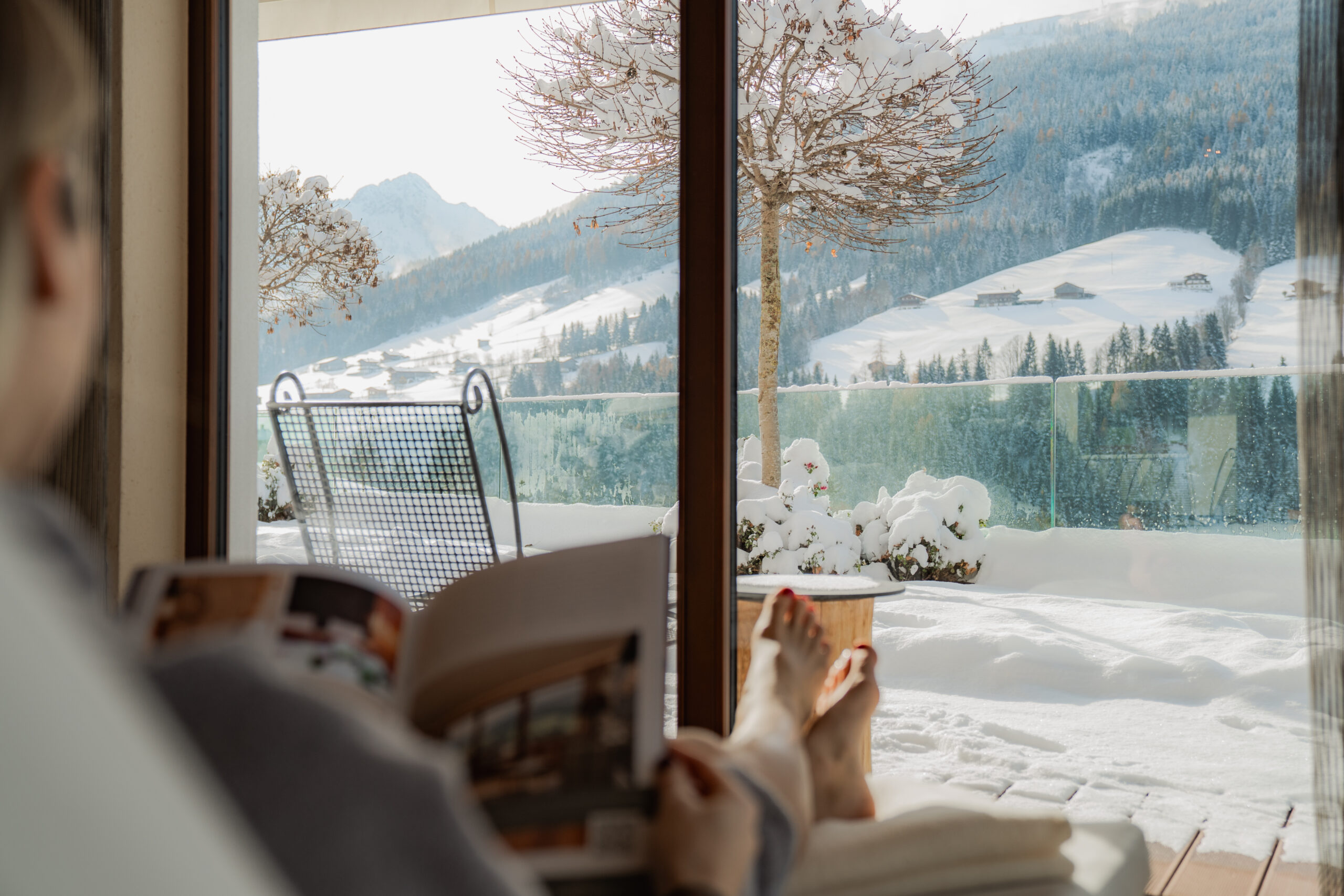 Frau auf Ruheliege genießt Ausblick auf Bergwelt aus Panoramafenster