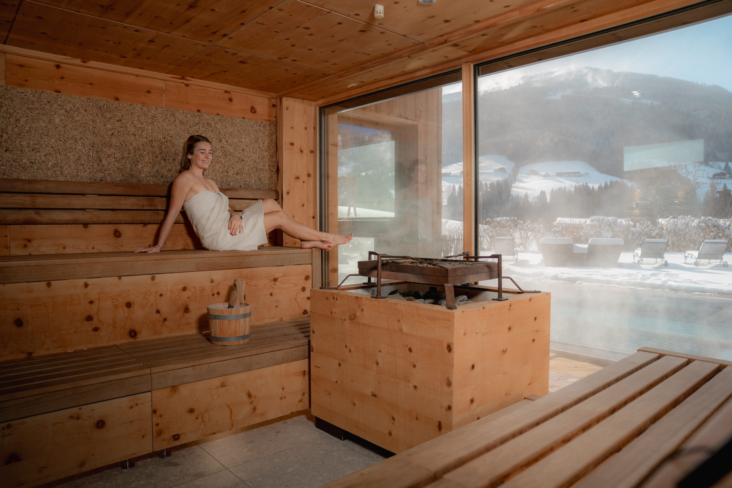Frau in Holzsauna mit Panoramablick auf verschneiten Garten mit Pool, Berge und das Alpbachtal