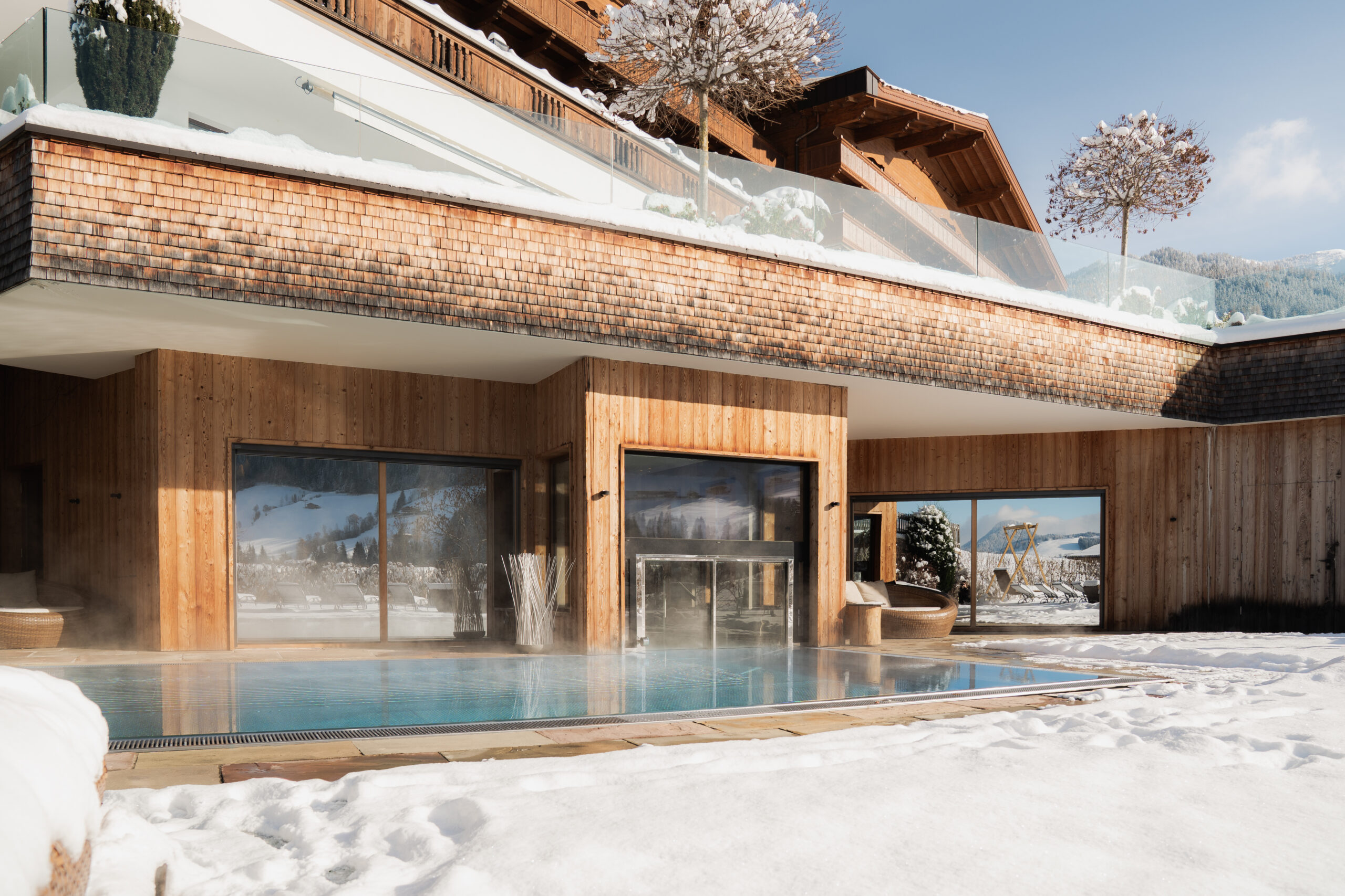 Outdoorpool und verschneiter Garten mit Hausansicht des Wellnesshotels Alpbacherhof im Alpbachtal