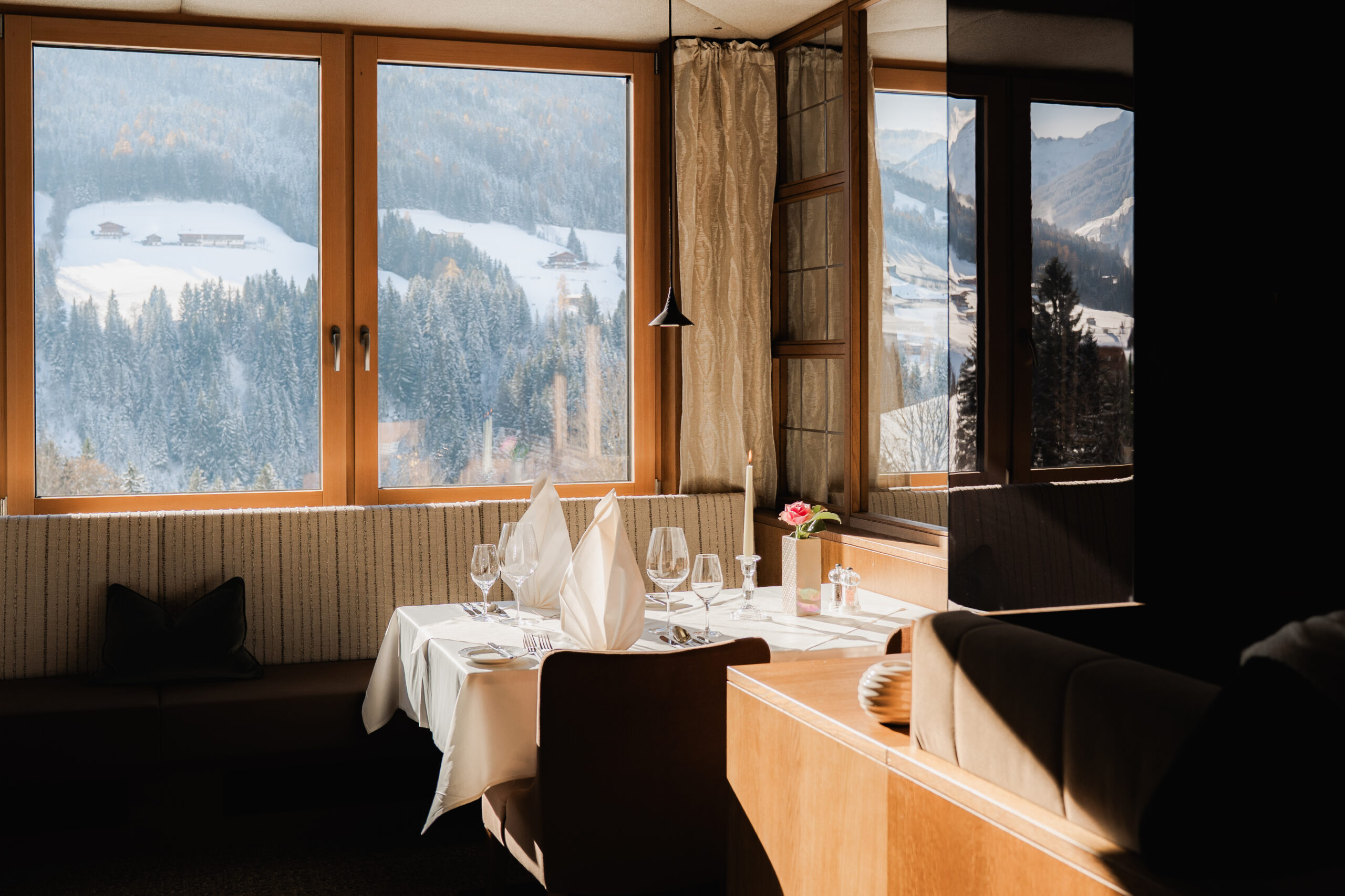 Paar stößt im Restaurant des Wellnesshotels Alpbacherhof an, im Hintergrund Panoramablick aufs verschneite Alpbachtal