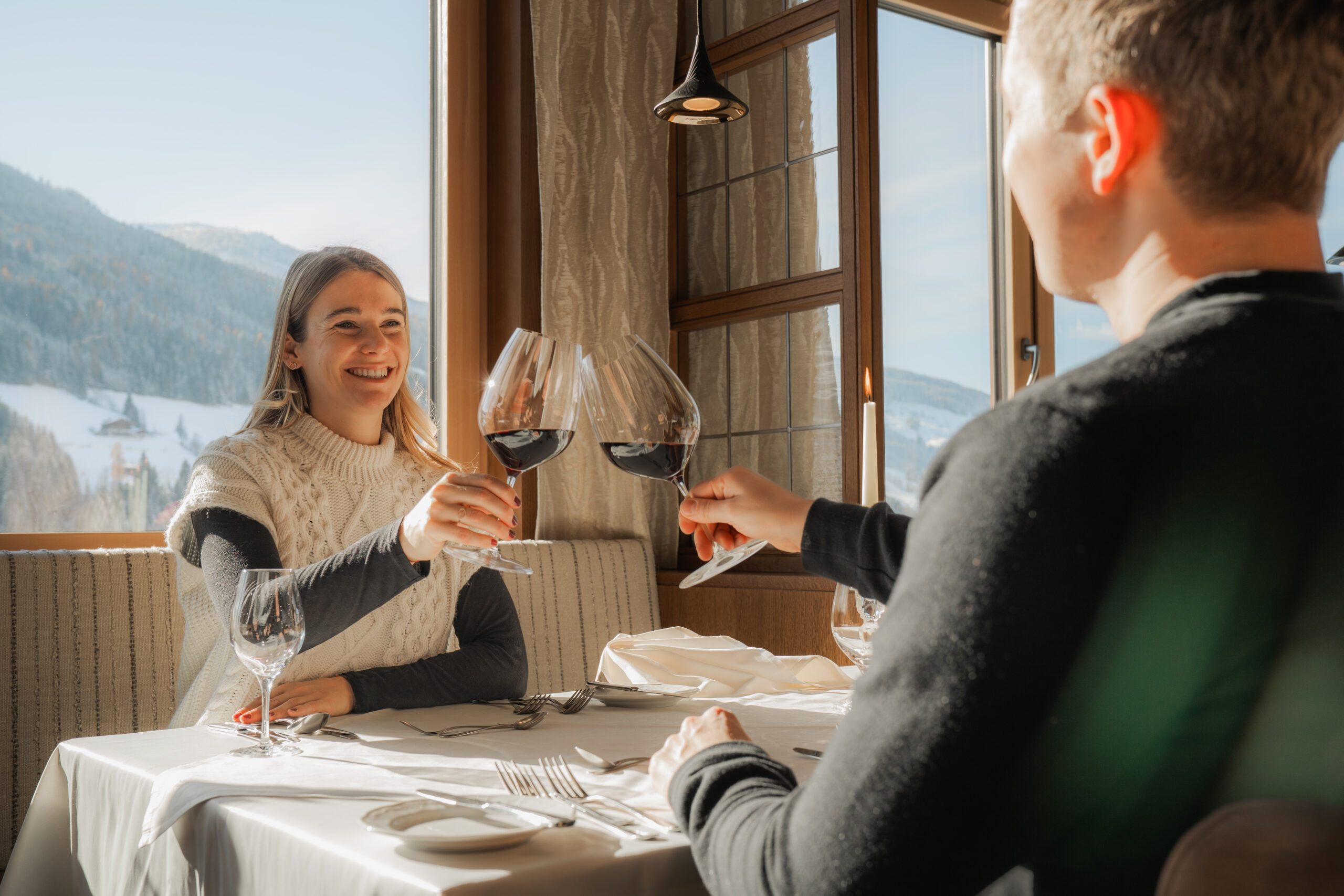 Paar stößt im Restaurant des Wellnesshotels Alpbacherhof an, im Hintergrund Panoramablick aufs verschneite Alpbachtal