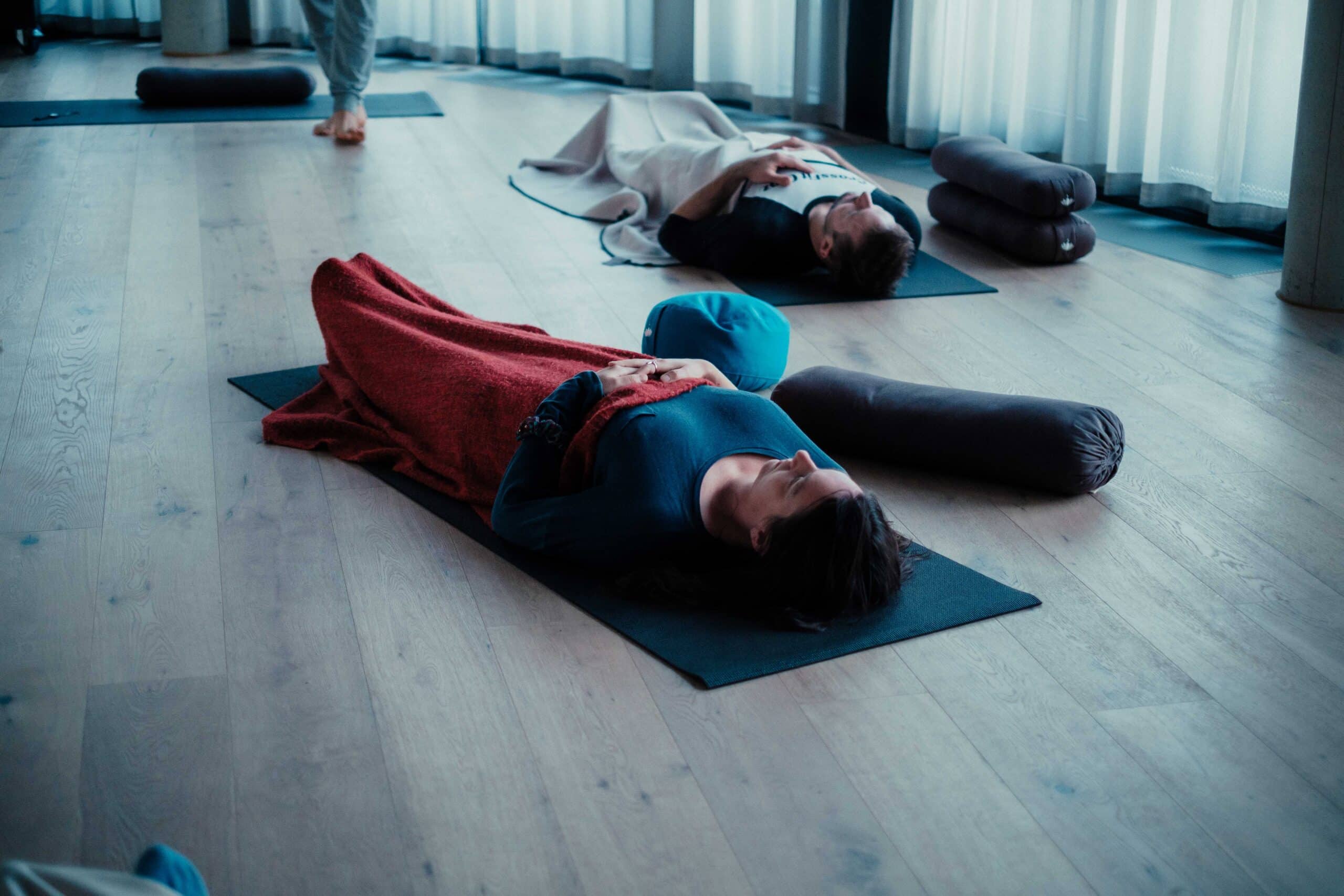 zwei Frauen liegen auf Gymnastikmatte, Atemtraining, mit Decke halb zugedeckt