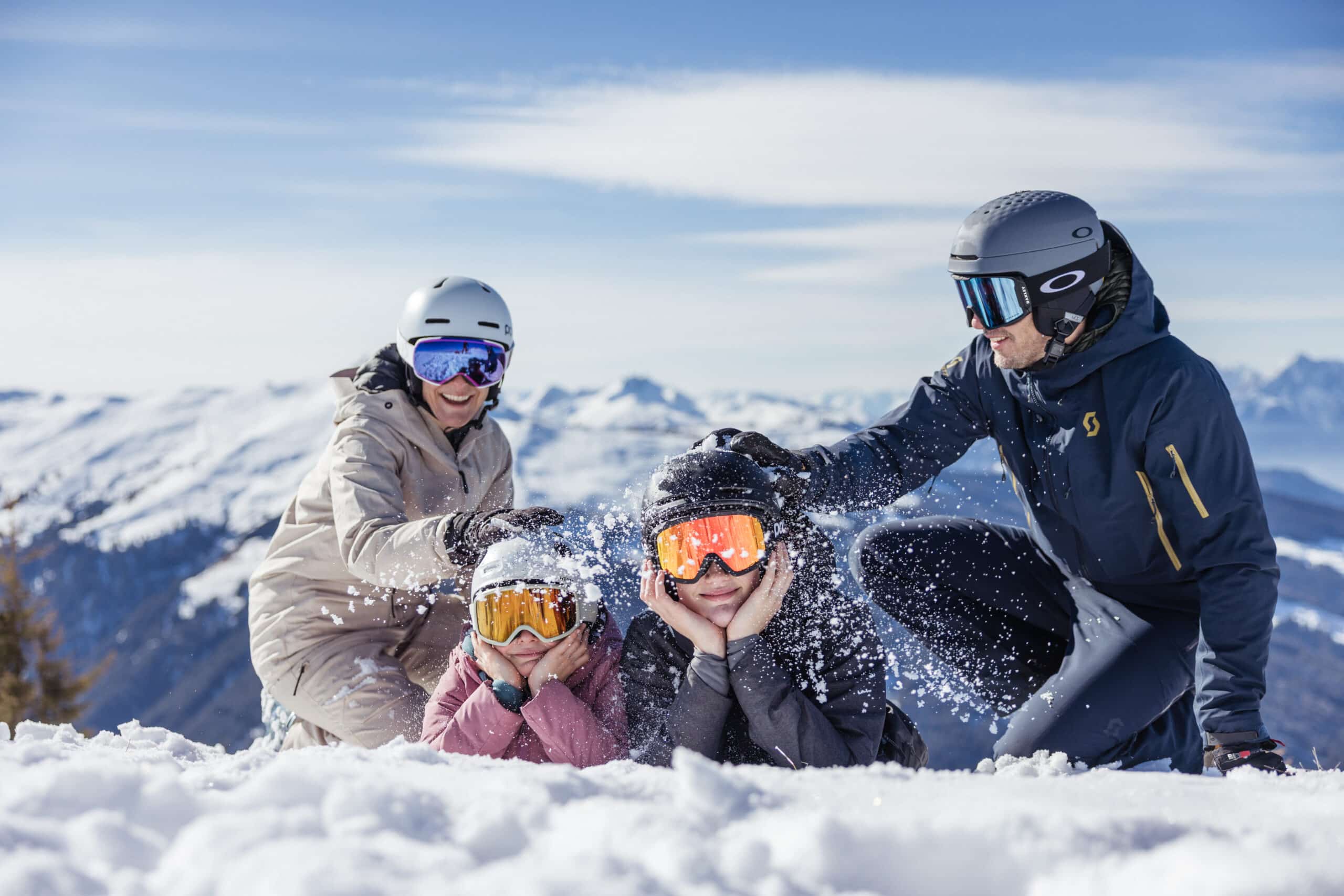 Winter Eltern mit 2 Kindern im Schnee mit Helm, Brille und Skianzug- haben spass, HIntergrund verschneite Berge, blauer Himmel